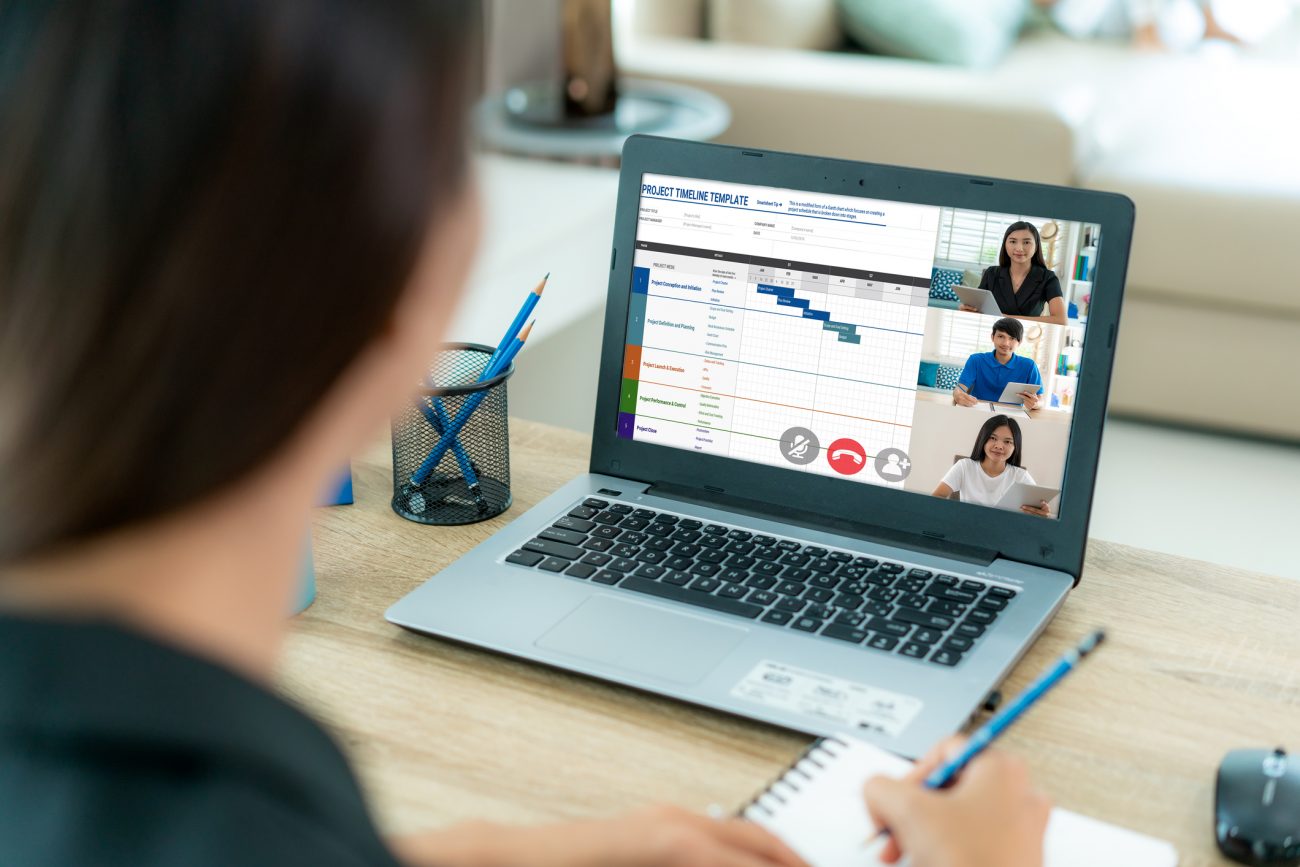 Back view of Asian business woman talking to her colleagues about plan in video conference. Multiethnic business team using computer for a online meeting in video call. Group of people smart working from home.
